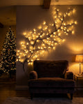 Willow vine light with warm LEDs on the wall above a velvet armchair beside a lit Christmas tree