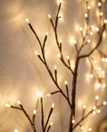 Close-up of dark brown twigs with small warm-white LEDs glowing against a plaster wall