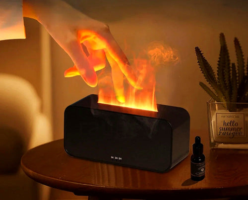Lueur flame effect diffuser with hand touching the flame mist, styled on a wooden side table with a plant and essential oil bottle