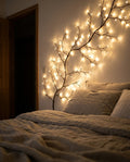 Willow vine light glowing warm white on the wall beside a bed at night